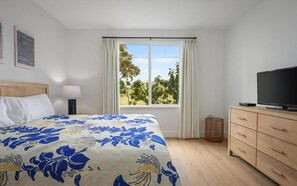 Une chambre à coucher avec un lit, une télévision, une commode et une fenêtre avec des rideaux.