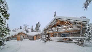 A log cabin with a porch and a chimney, surrounded by snow-covered trees. - Lapland Lodge (Kittilä)
