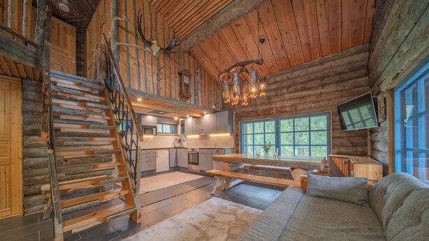A log cabin interior with a wooden staircase, a dining area, a sofa, and a kitchen. - Lapland Lodge (Kittilä)