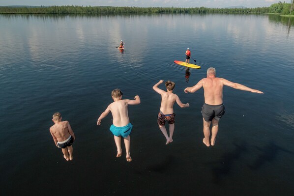 A group of people jumping into a calm lake surrounded by trees. - Lapland Lodge (Kittilä)