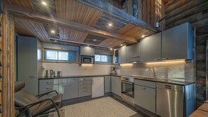 A modern kitchen with stainless steel appliances, wooden ceiling beams, and a window overlooking the snowy outdoors. - Lapland Lodge (Kittilä)