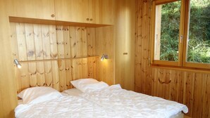 A wooden-paneled bedroom with a bed, two bedside lamps, and a window with a view of greenery. - Alluring apartment in Les Agettes (Les Agettes)