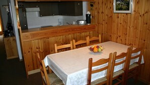 A wooden dining area with a table set for four, a fruit bowl on the table, and a kitchen area with a coffee maker and a sign warning of bears. - Alluring apartment in Les Agettes (Les Agettes)