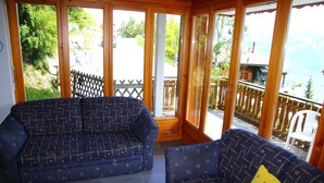 A room with two blue patterned sofas, a wooden table, and large windows offering a view of a wooden deck and greenery. - Alluring apartment in Les Agettes (Les Agettes)