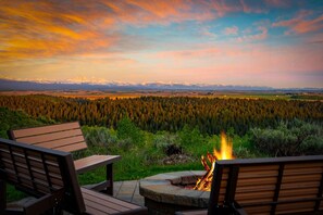 A deck with two wooden chairs overlooking a forest and a fire. - Cherry Butte Lodge| Luxe Lodge Sleeps 27, Hot Tub, Fire Pit, & Views! (Ashton)
