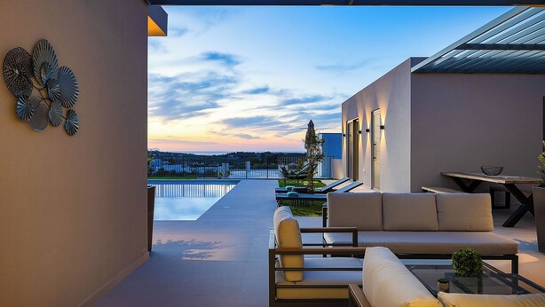A modern outdoor patio with a pool, seating area, and a view of the water and distant landscape.