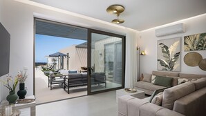 A modern living room with a sofa, a coffee table, and a dining area with a table and chairs. There is a sliding glass door leading to an outdoor patio.