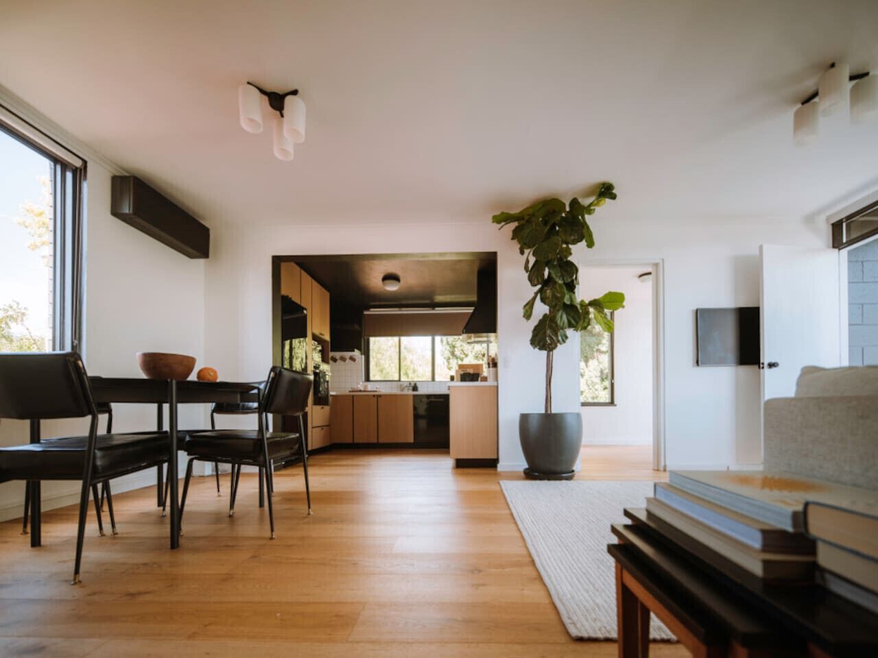 A modern kitchen with wooden cabinets, a dining area with a table and chairs, and a large potted plant.