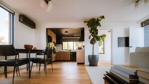 A modern kitchen with wooden cabinets, a dining area with a table and chairs, and a large potted plant. - The Perfect Apartment (Sandy Bay)