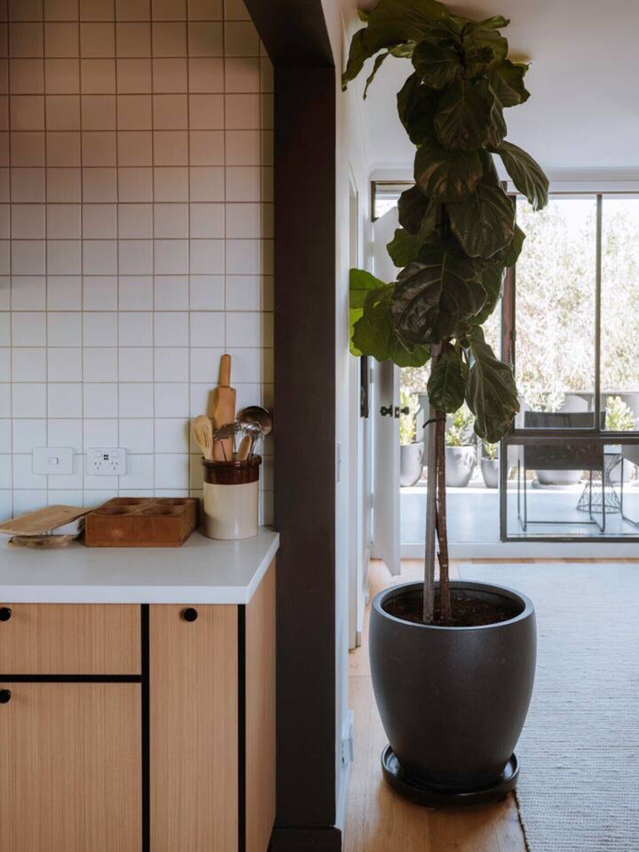 Een keuken met een potplant, een houten snijplank en een houder voor keukengerei.