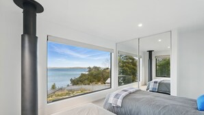 Ein Schlafzimmer mit einem großen Fenster und Blick auf einen See und Bäume.