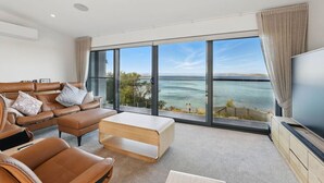 Ein modernes Wohnzimmer mit einem großen Fenster und Meerblick, einer Ledersofa, einem Couchtisch und einem Flachbildfernseher.