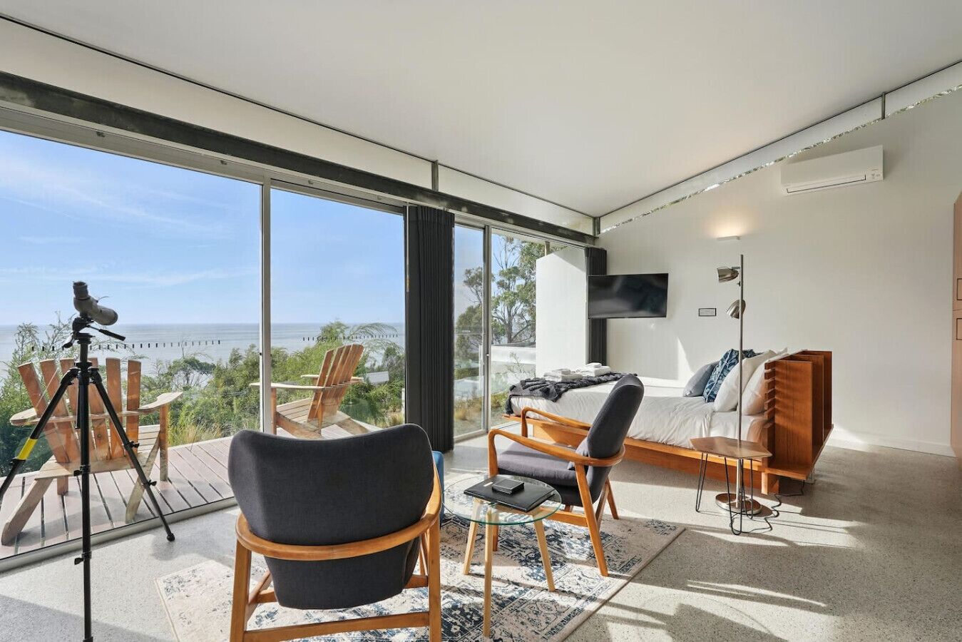 Una sala moderna con un ventanal que ofrece vistas panorámicas, un telescopio en una terraza y una zona de estar acogedora con un sofá y sillones.