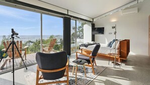 Un salon moderne doté d’une grande fenêtre donnant sur un paysage magnifique, d’un télescope installé sur une terrasse et d’un coin salon confortable avec un canapé et des fauteuils.
