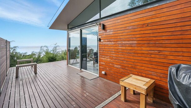 Une terrasse extérieure moderne avec un plancher en bois, une porte vitrée donnant sur un balcon et une vue sur la mer.