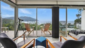 Une pièce moderne avec de grandes fenêtres, un trépied, deux chaises en bois, une petite table et un canapé.