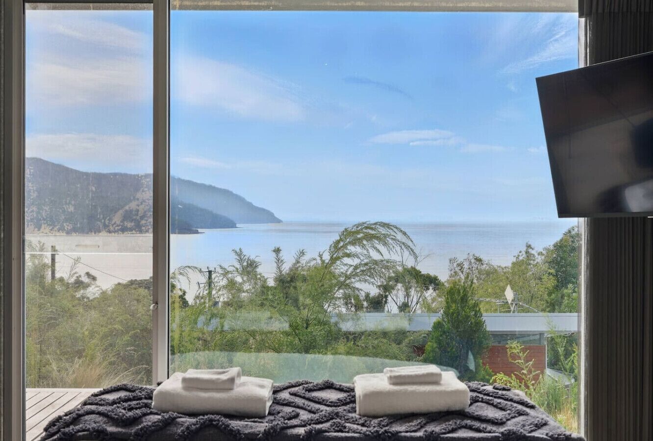 A room with a large window overlooking a beach and ocean. There are two towels on a dark rug.