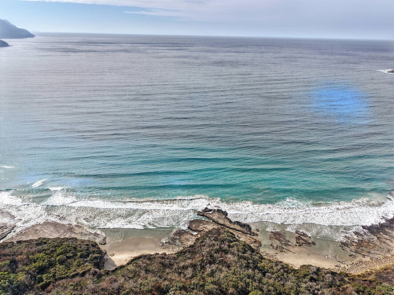 A coastal landscape with a beach, rocky outcrops, and a view of the ocean.