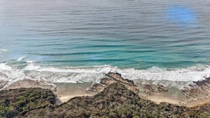 Een kustlandschap met een strand, rotsachtige uitstekenissen en uitzicht op de oceaan.
