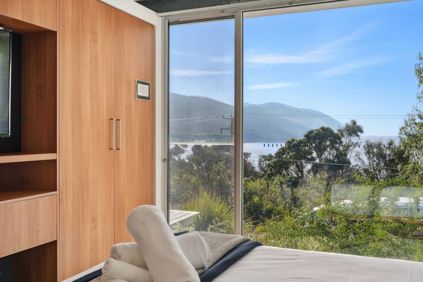 A bedroom with a large sliding glass door leading to a scenic view of a body of water and mountains.