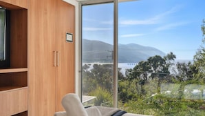 Een slaapkamer met een groot schuifglasraam dat uitkomt op een mooi uitzicht over een waterpartij en bergen.