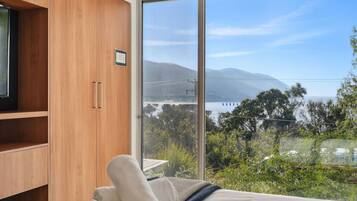 A bedroom with a large sliding glass door leading to a scenic view of a body of water and mountains.