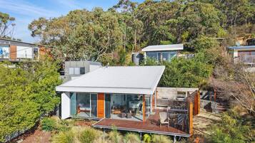A modern house with a large deck, surrounded by dense vegetation and trees.