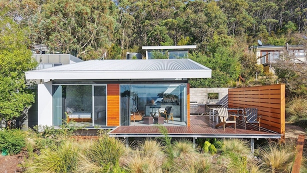 Een modern huis met een terras, grote glasramen en uitzicht op een beboste helling.