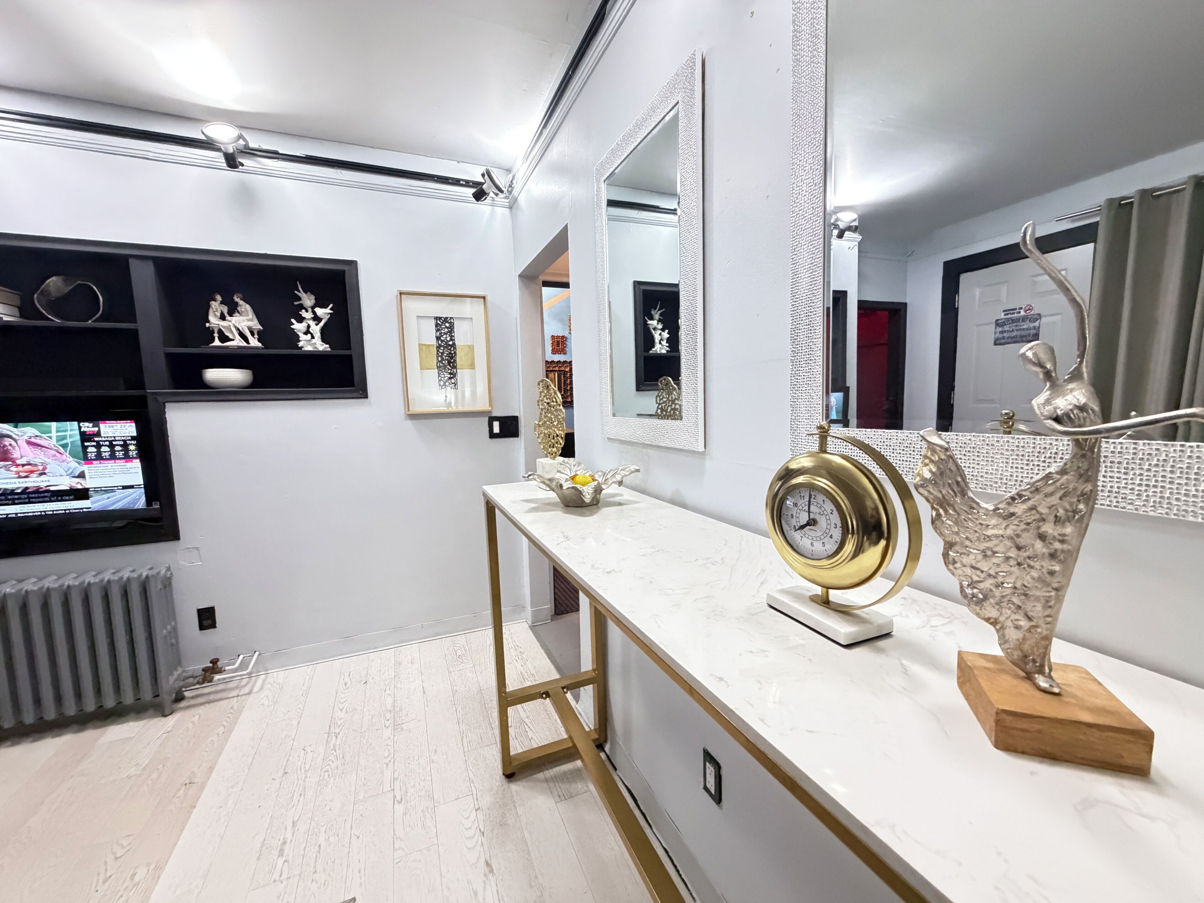 Un baño moderno con un tocador blanco, un reloj con marco dorado y una escultura decorativa.