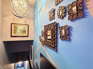 Un couloir agrémenté d’un lustre, de tableaux encadrés et de miroirs décoratifs fixés au mur.
