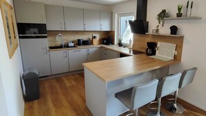 A modern kitchen with grey cabinets, a wooden countertop, and a black range hood. There are two bar stools and a small island with a sink. - Chalet on the Diemelsee with lake view, sun terrace and much more. Pet friendly (Diemelsee)