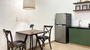 A modern kitchen with a dining area, featuring a wooden table, chairs, a hanging light fixture, a refrigerator, and a green countertop. - NAMTO HOUSE PARK HAN MARKET 3A (Đà Nẵng)