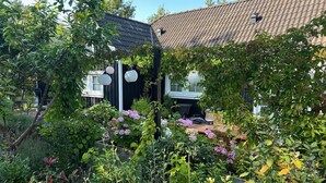 A garden with a wooden table and chairs, surrounded by various plants and flowers. - Cozy holiday home in scenic Rågeleje (Vejby)