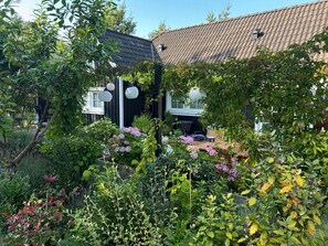 A garden with a wooden table and chairs, surrounded by various plants and flowers.