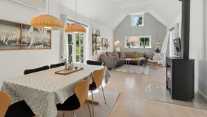 A spacious living area with a dining table, chairs, a sofa, a fireplace, and a large window. - Cozy holiday home in scenic Rågeleje (Vejby)
