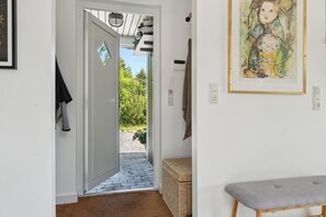 A hallway with a door leading to an outdoor area, a bench, and a framed artwork on the wall.