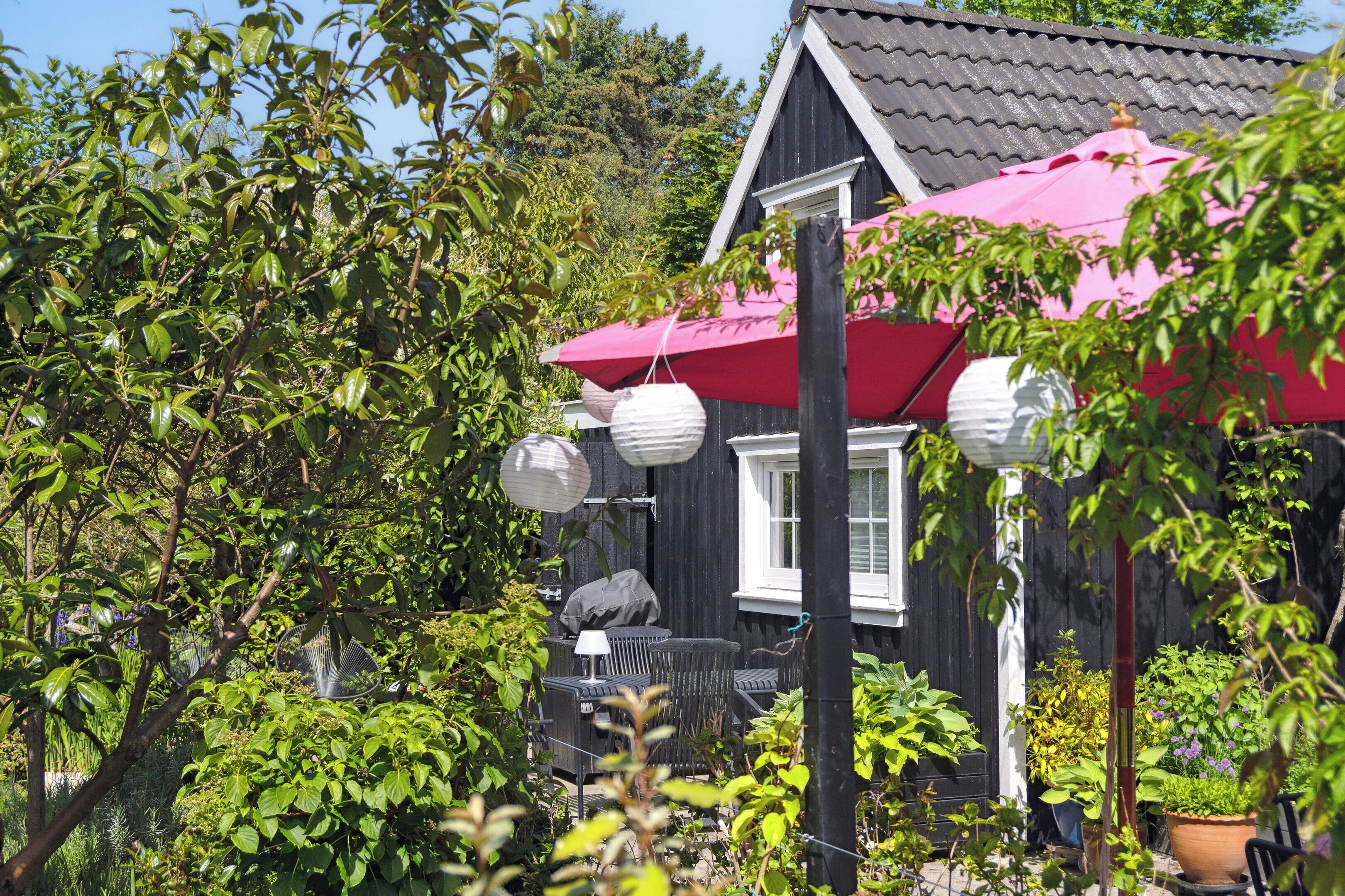 A wooden house with a red roof, a patio with outdoor furniture, and hanging paper lanterns.