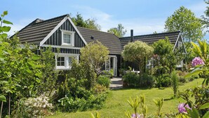 A house with a sloped roof, surrounded by a well-maintained garden with various plants and flowers. - Cozy holiday home in scenic Rågeleje (Vejby)