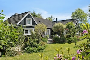 A house with a sloped roof, surrounded by a well-maintained garden with various plants and flowers.