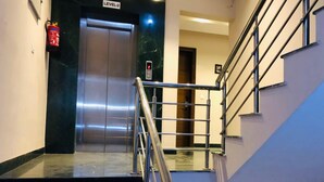 A modern elevator with a digital display, a fire extinguisher, and a staircase with metal railings. - Moti Mahal Inn (Haldwani)