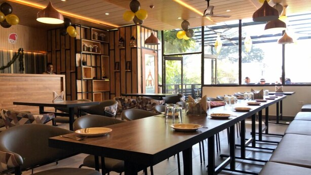 A restaurant with long communal tables, black chairs, and pendant lighting. - Moti Mahal Inn (Haldwani)