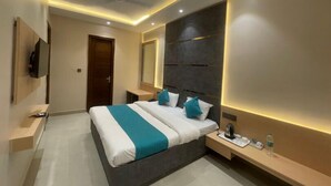 A modern bedroom with a large bed, bedside tables, a TV, and a mirror. - Moti Mahal Inn (Haldwani)