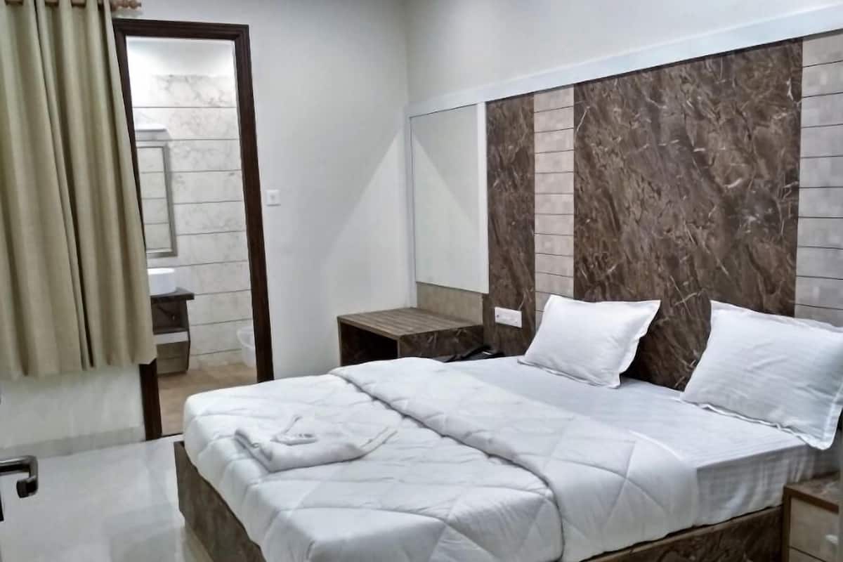Quarto de hotel moderno com cabeceira de mármore, cama bem arrumada, mesa de cabeceira de madeira e um banheiro visível por uma porta aberta.