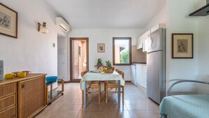 Eine kleine Küche mit Esstisch, Stühlen, Kühlschrank und einem Bett.