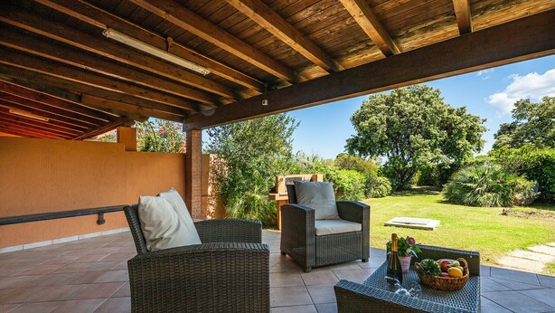 Eine Terrasse im Freien mit Korbmöbeln, einem Tisch mit Obstschale und Flaschen sowie Blick auf einen Garten.