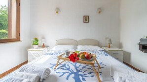 Ein Schlafzimmer mit einem Bett, zwei Nachttischen, einem Fenster und einem Tablett mit Früchten und Blumen.