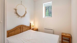 A bedroom with a wooden headboard, a round wall decoration, a bedside lamp, a small window, and a radiator. - Apartment in Saint-Sorlin near Ski Resort (Saint-Sorlin-d´Arves)