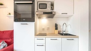 A compact kitchen with a microwave, oven, and built-in stove. There is a sink with a faucet and a countertop with a knife block. - Apartment in Saint-Sorlin near Ski Resort (Saint-Sorlin-d´Arves)
