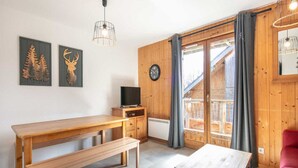 A cozy room with a wooden bench, a small table, a TV, and a window with curtains. - Apartment in Saint-Sorlin near Ski Resort (Saint-Sorlin-d´Arves)