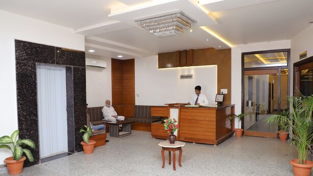 A hotel reception area with a receptionist, a reception desk, a seating area, and potted plants. - Hotel The Golden Bird (Agra)